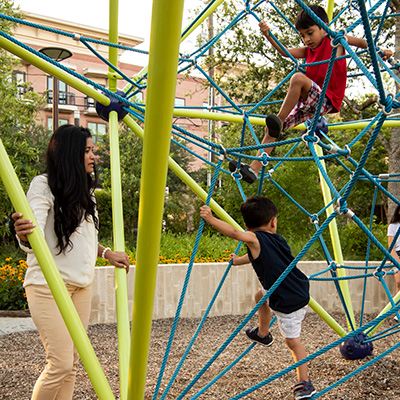 Mother plays with children climbing on playground ropes