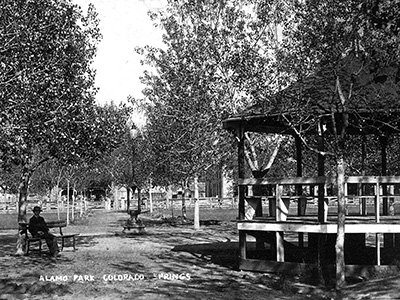 Trees are prominent in this historic photo of man sitting on a bench near the gazebo