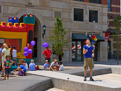 Colorful party in a plaza with man juggling and children playing by a bouncy house