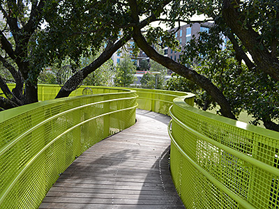 A walkway with bright yellow-green railings follows a winding path through trees