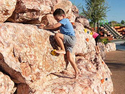 Young boy ascends a playground climbing wall on a bright sunny day